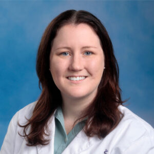 dr mccarthy's headshot smiling at camera with blue background and white coat