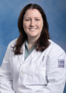 dr mccarthy's portrait smiling at camera with blue background and white coat