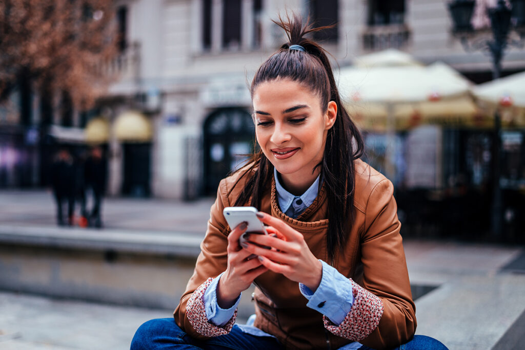 Mujer joven enviando mensajes de texto en el smartphone mientras está sentada en la plaza de la ciudad.