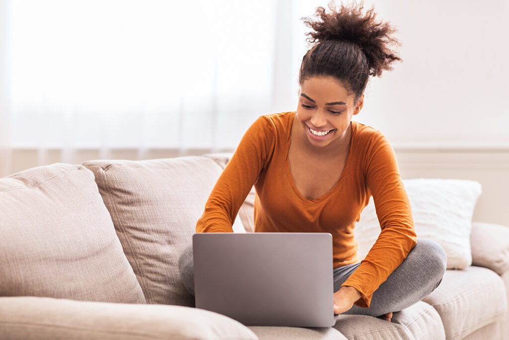 Dama feliz usando el ordenador portátil trabajando desde casa sentada en el sofá