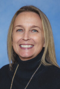 Sharon Obadia's smiling portrait with blue background and long blonde hair with black turtleneck