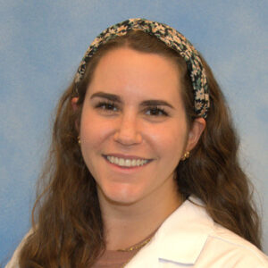 Dania's headshot with blue background in white coat and long hair with headband