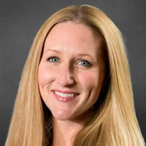 Kelly's smiling headshot with long blond hair and grey background