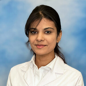 Dr Kaur's headshot in white coat and dark hair pulled back