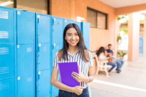 Student smiling while holding books in hallway