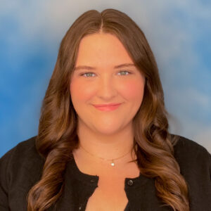 Carrie's smiling headshot with long brown hair, black top, and blue background