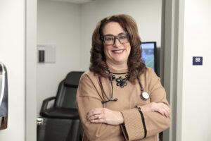 Dr. Thomas smiling portrait with tan top and arms crossed standing in patient room door frame