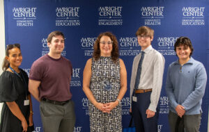 summer interns who won the capstone project posing with dr thomas in front of our logo banner