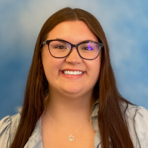 Isabella's smiling headshot with long brown hair, glasses, and blue background
