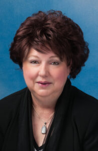 Mary's smiling headshot with short brown hair and blue background