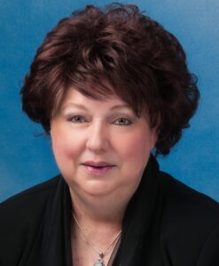 Mary's smiling headshot with short brown hair and blue background