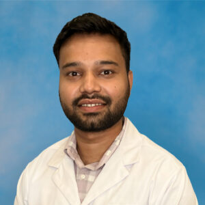 Naman's smiling headshot with blue background and white jacket
