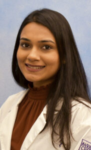 Prachi's smiling headshot with blue background and white jacket