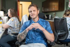 man sitting on chair talking with in blue shirt staring at the camera