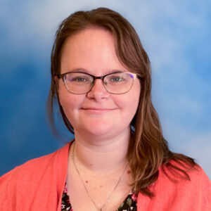 Susan's smiling headshot with glasses, pink top, and blue background