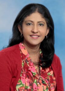 Dr. Manju Mary Thomas smiling portrait with blue background and red top and long dark hair
