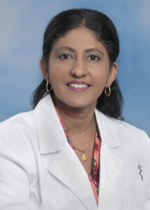 Dr Manju Mary Thomas' smiling headshot with blue background and white coat