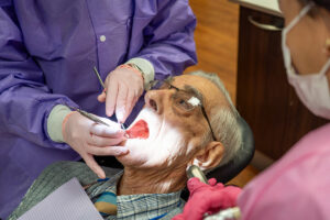 patient laying in dental chair getting his mouth checked by dental care team