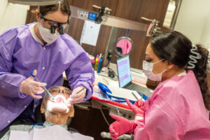 patient laying in dental chair getting his mouth checked by dental care team