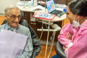 gentleman with glasses and sweater vest sitting in dental chair smiling at his hygienist