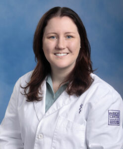 Caitlyn's smiling headshot with blue background and white coat