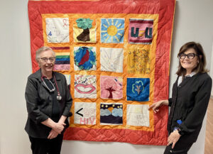 AIDS quilt with many patches and different colors with sister ruth standing next to it