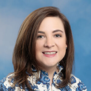 Kathleen's smiling headshot with blue headshot and blue and white dress