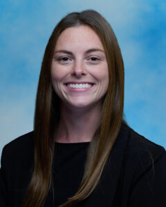 Catherine Nealon's smiling portrait with blue background and long brown hair