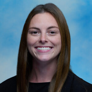 Catherine Nealon's smiling headshot with blue background and long brown hair
