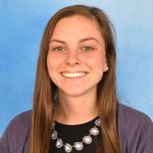 Catherine Nealon's smiling headshot with blue background and long brown hair