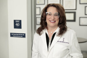 Dr. Linda Thomas-Hemak's portrait with white coat and glasses standing in a doorway