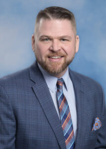 Brian's smiling portrait with blue background and blue plaid suitcoat