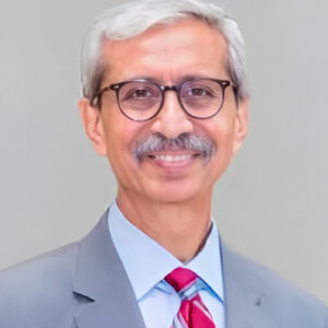 Headshot of board member Nasruddin Rupani smiling with glasses and grey suit and red striped tie