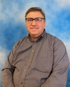 Dr. Henry Novroski's headshot with a checked button down shirt