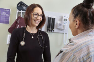 Stephanie Tanona, in a black shirt, interacts with a patient who is sitting in a patient room