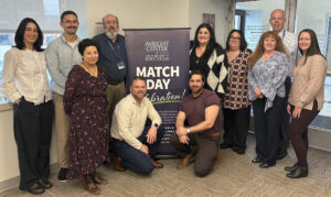 Group photos of gme staff members posing next to a happy match day banner