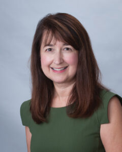 Headshot of Dr. Mary Louise Decker in green dress and long brown hair