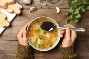 a woman's hands are holding a bowl of soup at a table