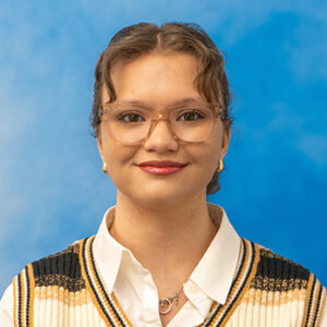 Aurora's headshot with blue background and glasses and striped v-neck sweater
