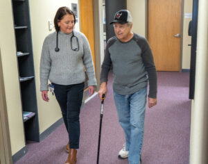 Mallory Racoski, a board-certified physician assistant, walks patient Elmer “Butch” Richie down the hallway