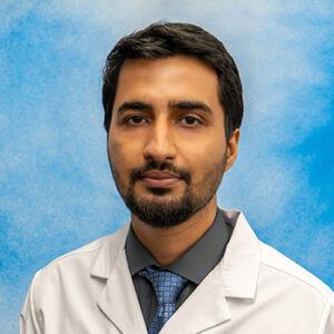 IM-Geri resident Abdullah Minhas headshot in white coat and on blue background