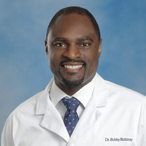 IM resident Bobby Birhiray headshot in white coat and on blue background