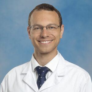 IM resident Joseph Malek headshot in white coat and on blue background