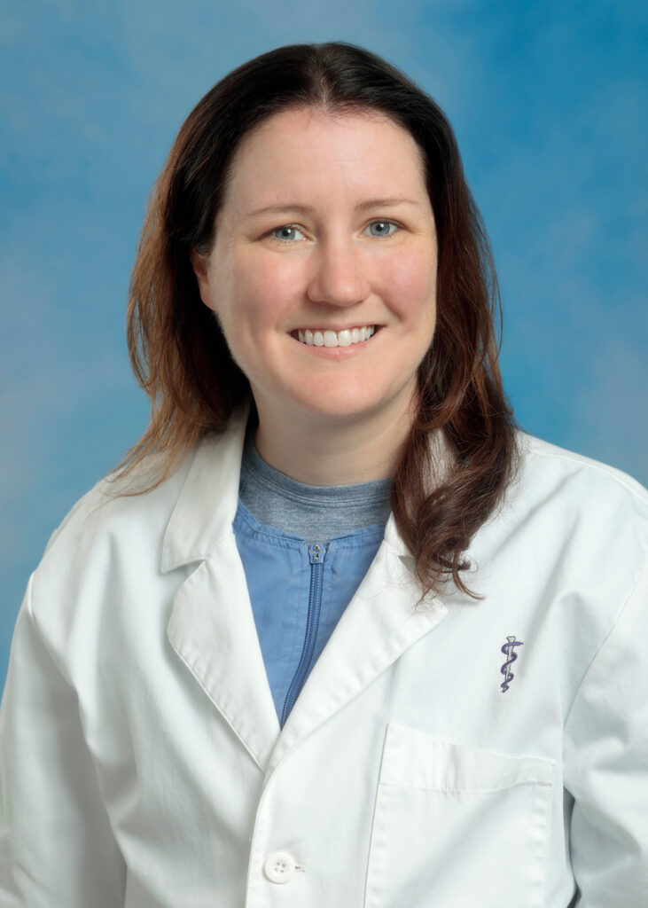 Caitlyn's smiling headshot with blue background and white coat